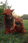 Two children in tiger-striped outfits playing on grass.
