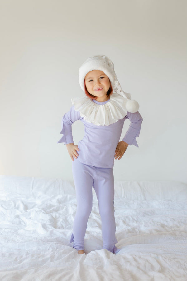 Child wearing a purple outfit with a white ruffled collar and matching hat on a white background