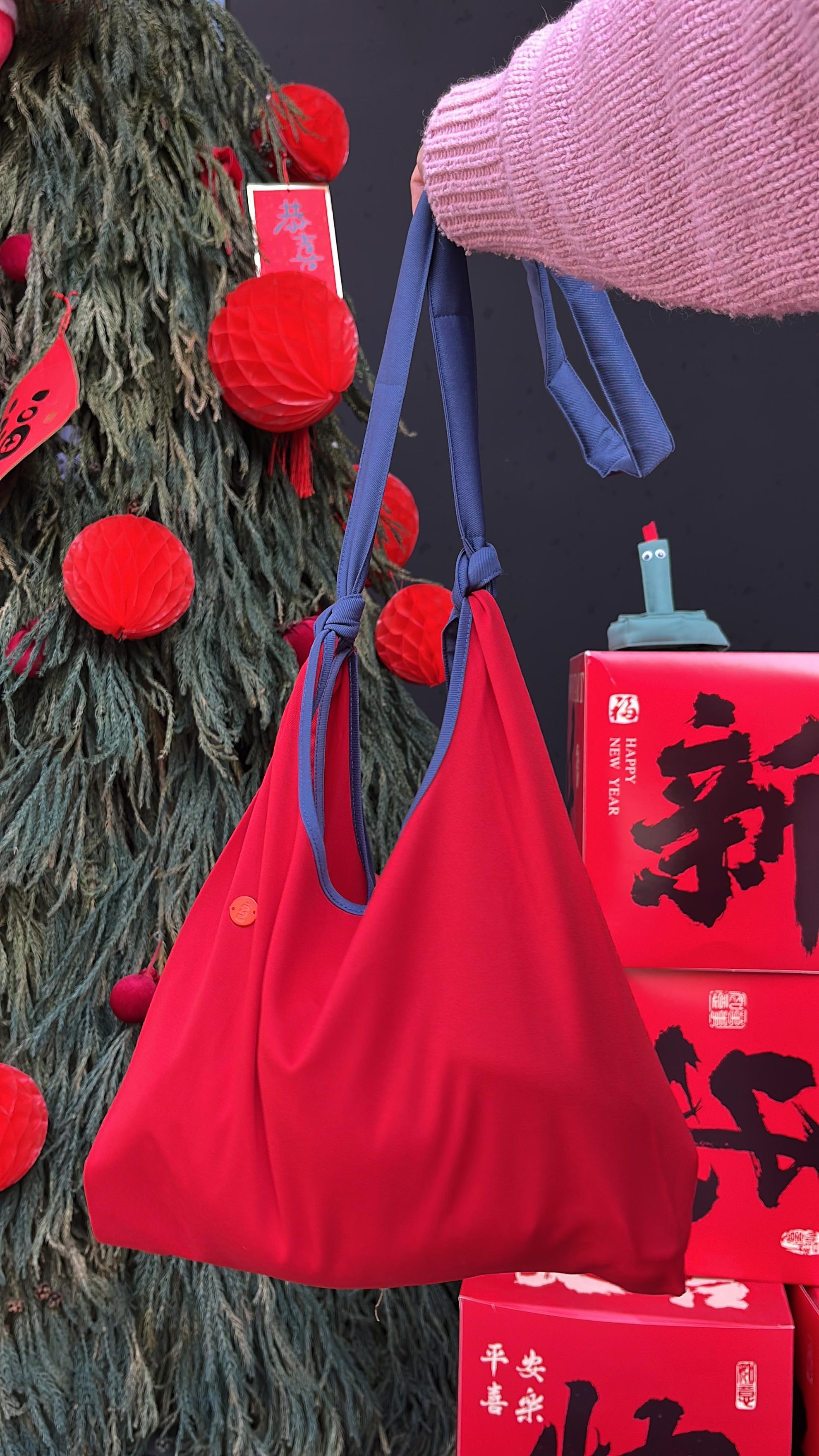 Red bag held by a person with a decorated tree and red boxes in the background