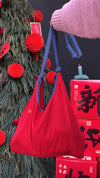 Red bag held by a person with a decorated tree and red boxes in the background