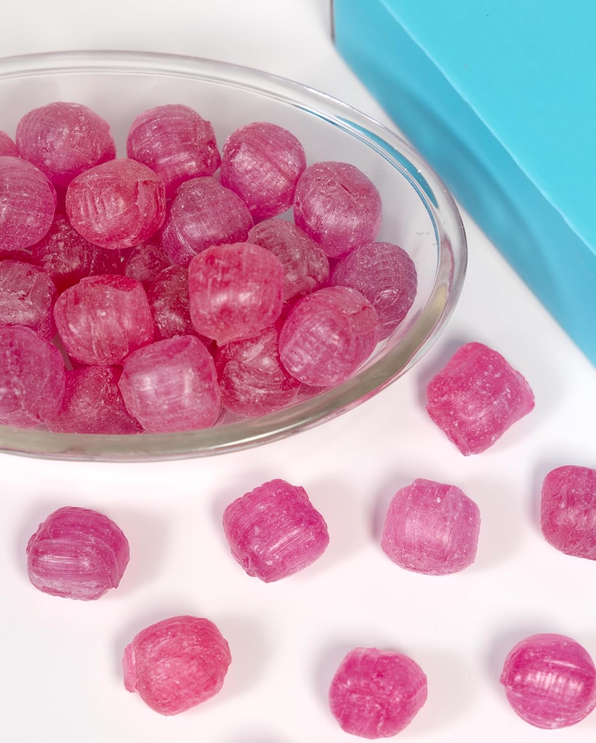 Pink gummy bears in a glass bowl with a blue container on a white background