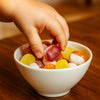 Child's hand reaching into a bowl of colorful gummy candies on a wooden table.