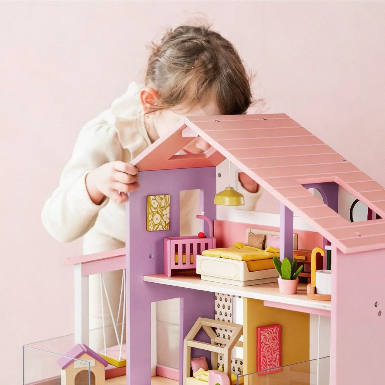 Child playing with a pink and purple dollhouse against a light pink background