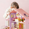 Child playing with a pink and purple dollhouse against a light pink background
