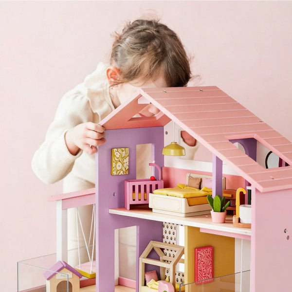 Child playing with a pink and purple dollhouse against a light pink background