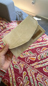 Beige pouch held by a hand on a patterned fabric background