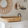 Woven basket with black handles on a white surface, with decorative wall art and toys in the background.