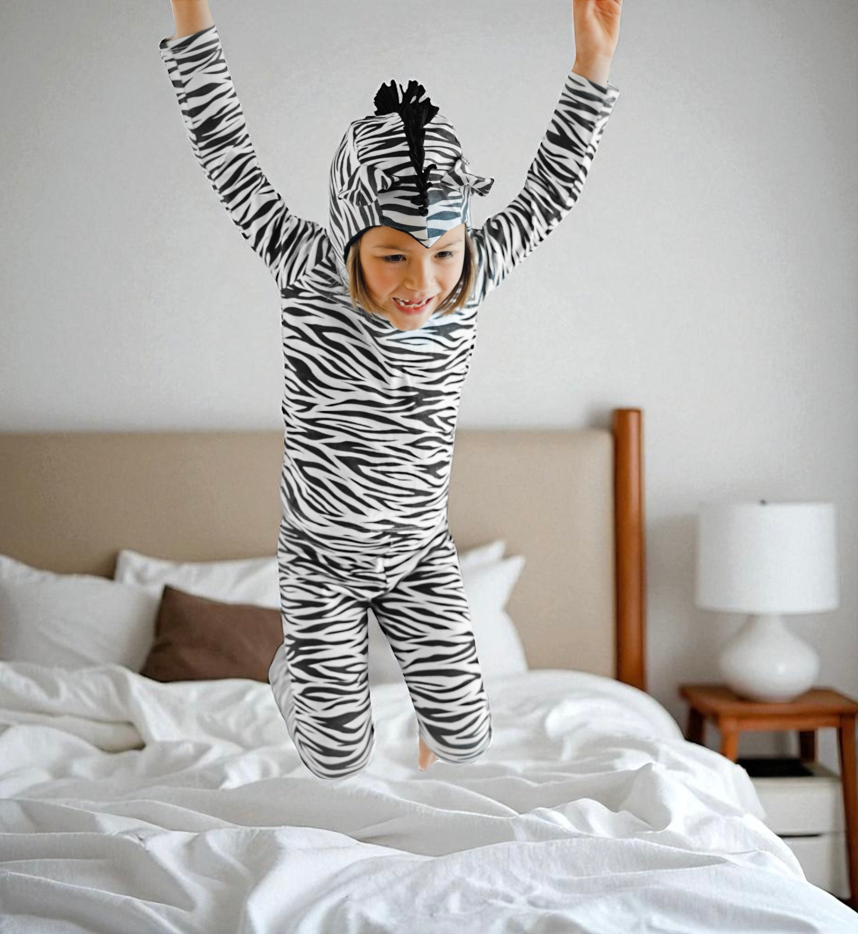 Child in zebra-striped pajama jumpsuit jumping on a bed in a bedroom.