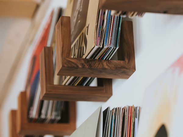 Wooden record holder with vinyl records on a white wall.
