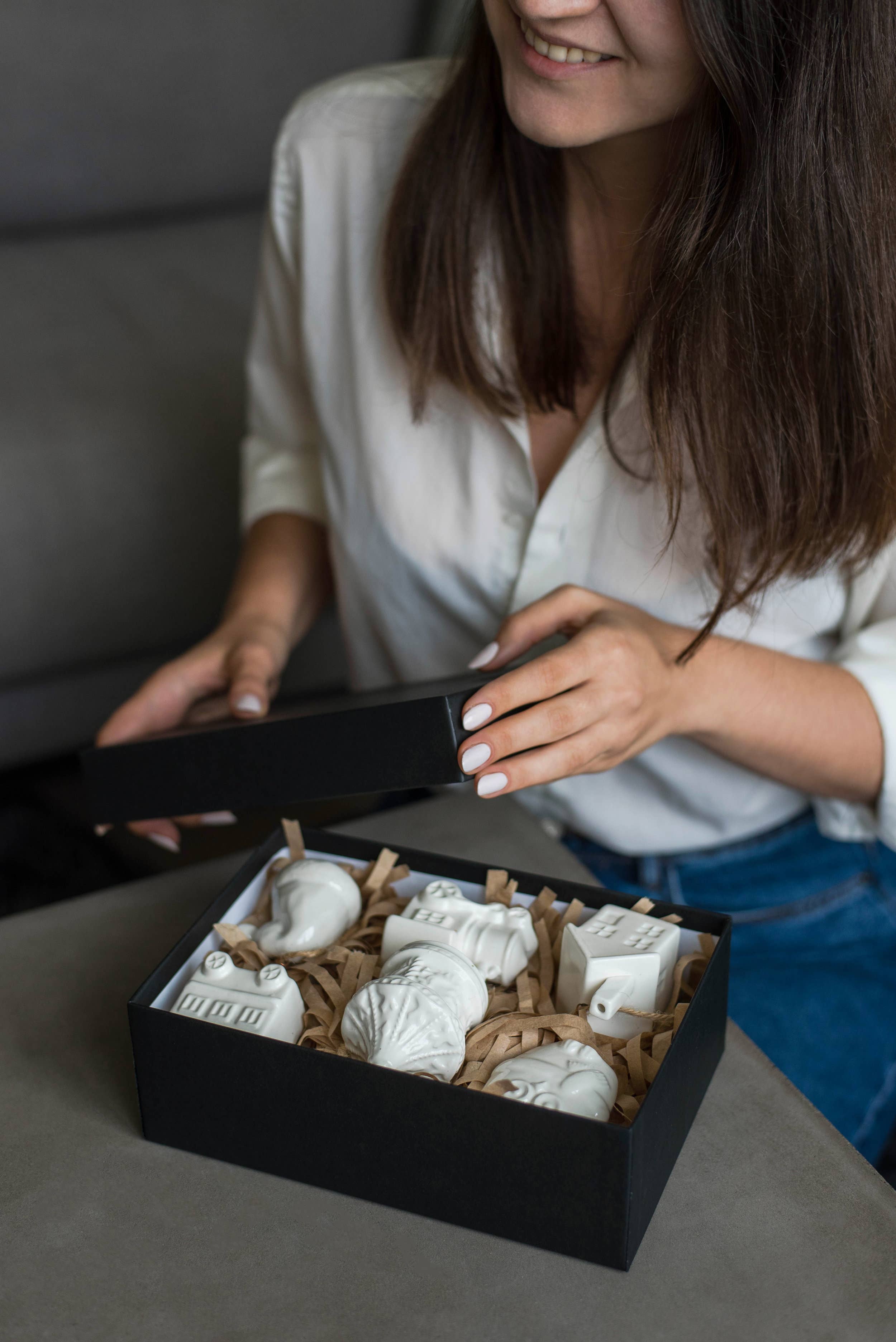 Person opening a black box containing decorative items on a gray surface.