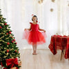 Child in a red dress standing next to a decorated Christmas tree in a festive room.