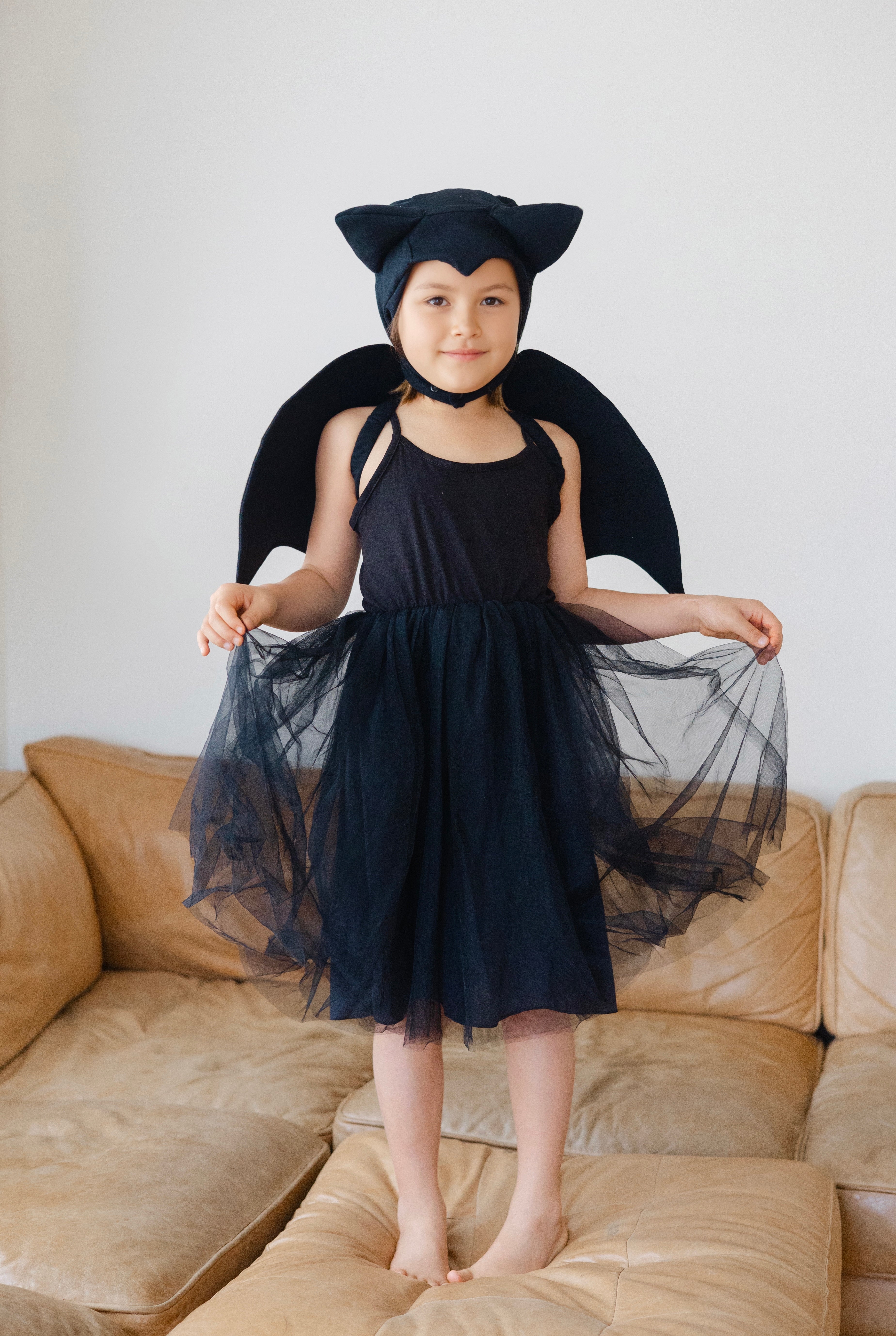 Child in a black cat costume standing on a beige couch against a white wall