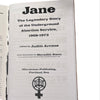 Inside spread of the Jane zine open to body text, showing the story of the Jane Collective, on a wooden surface