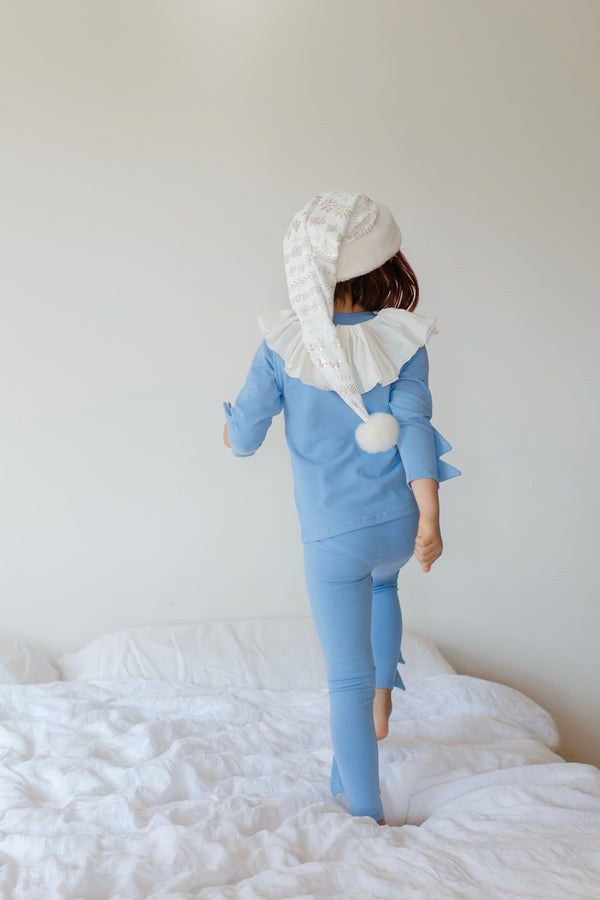Person wearing a blue outfit with a white hat and scarf on a white bed.