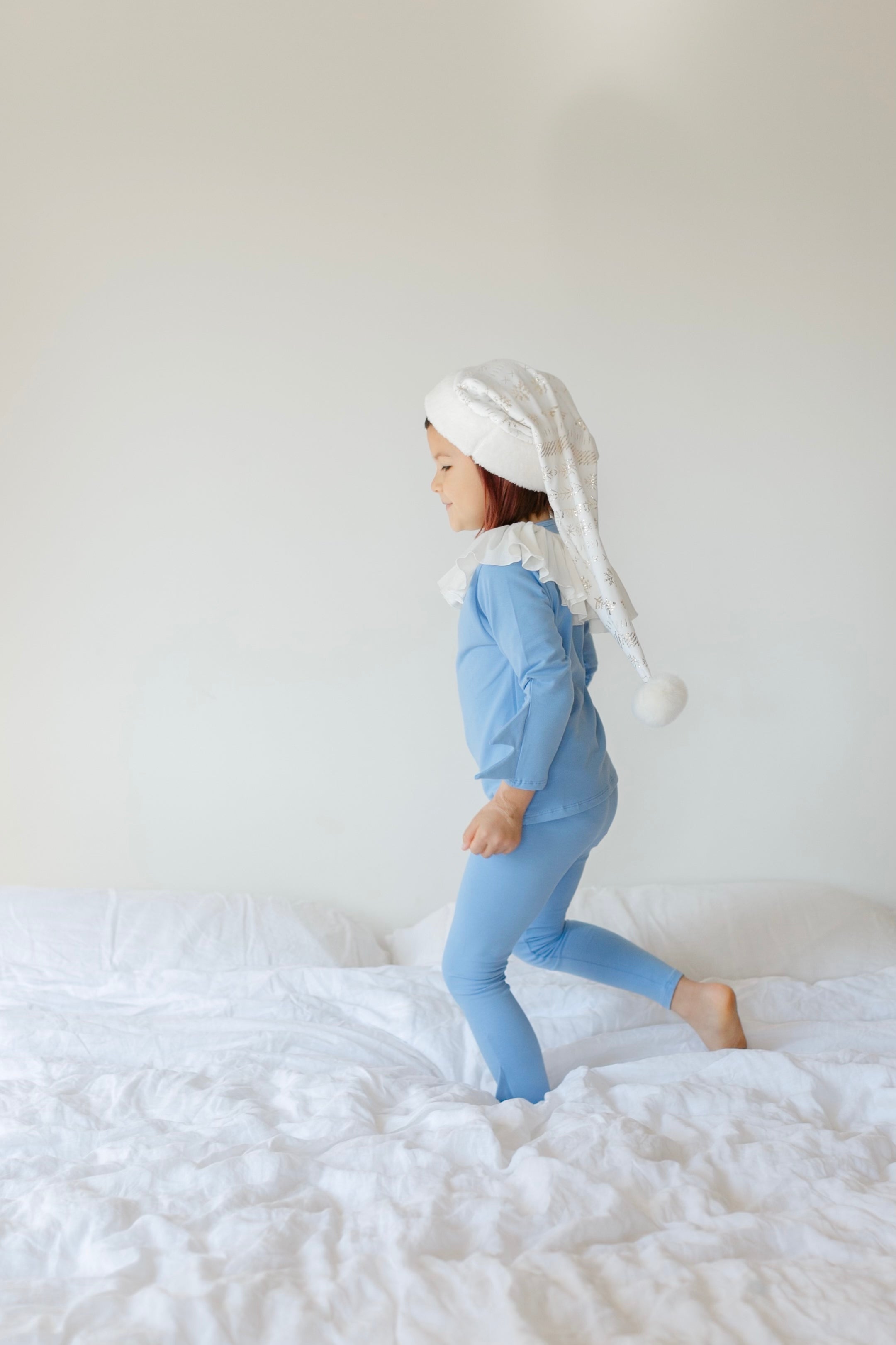 Child wearing a blue outfit and white headscarf on a white bed