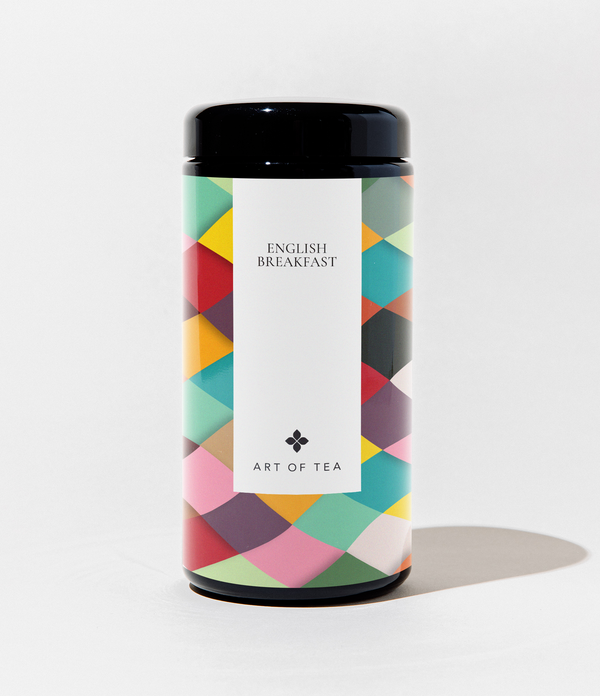 A cylindrical canister of Art of Tea English Breakfast tea, featuring a colorful geometric pattern in shades of teal, pink, yellow, and red, with a white central label and a black lid, set against a plain white background.