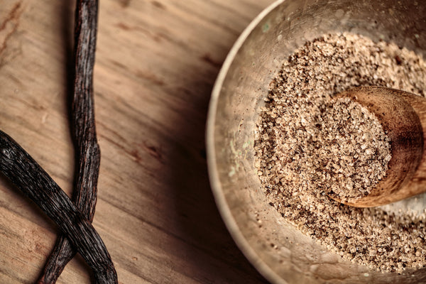 Vanilla beans and ground vanilla powder in a bowl on a wooden surface