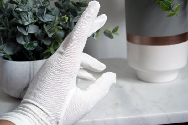 White gloves on a marble surface with a plant and vase in the background