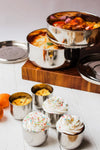Metal containers with food on a wooden stand and white surface with cupcakes.