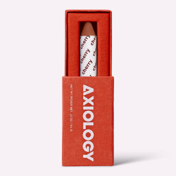 Axiology lip balm in a red box on a white background. Axiology's award-winning Balmie crayon — vegan, plastic-free & handmade in the USA. Multi-use color for lips, eyes & cheeks. On Oprah's Favorite Things List. Shop now.