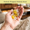 Hand holding two wrapped candies with 'Andy Anand' branding, set against a blurred indoor background.