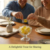 Two people sharing a bowl of yellow candies on a wooden table.