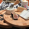 Wooden cheese board with assorted cheeses and figs on a table with a candle in the background.