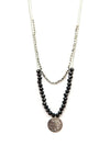 Two layered necklaces on a white background, one with black beads and a silver pendant, the other with smaller beads.
