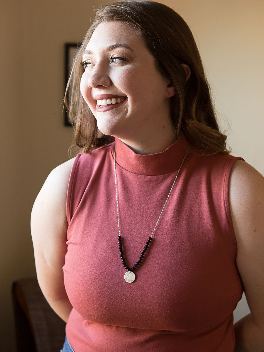 Black beaded convertible necklace worn as a single strand with hammered silver pendant by Fair Anita
