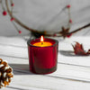 Red candle in a glass holder on a wooden surface with decorative elements.