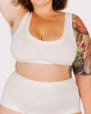 Person wearing a white sports bra and shorts set with tattoos visible on arms.