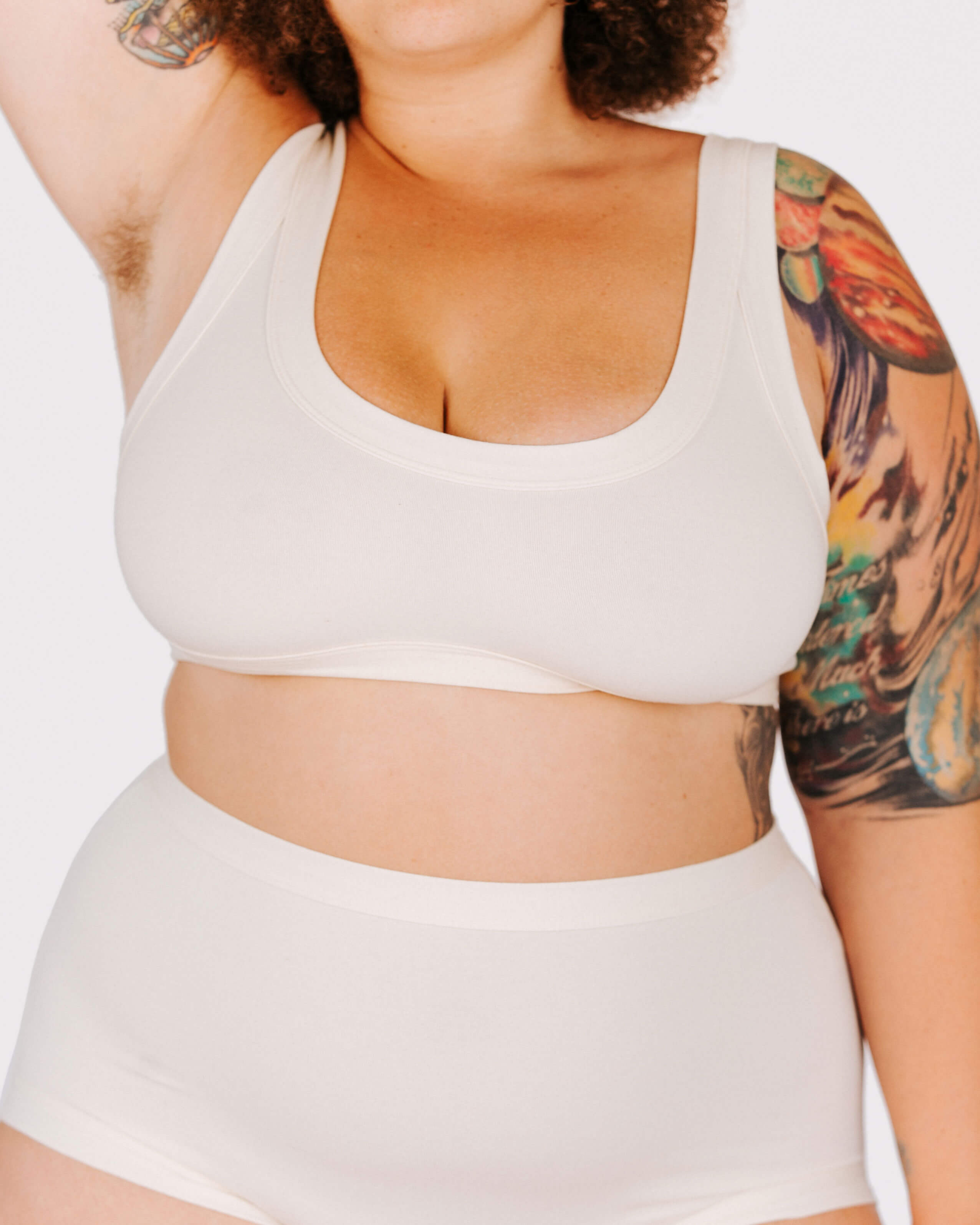 Person wearing a white sports bra and shorts set with tattoos visible on arms.