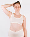 Woman wearing a white tank top and underwear set against a plain background