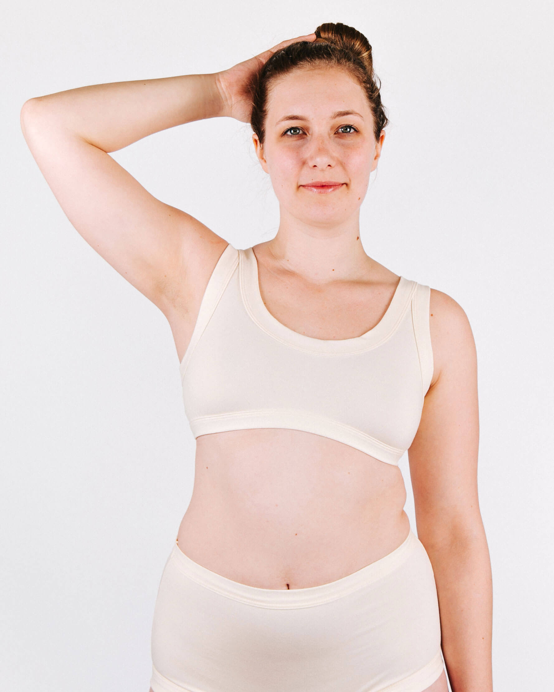 Woman wearing a white tank top and underwear set against a plain background