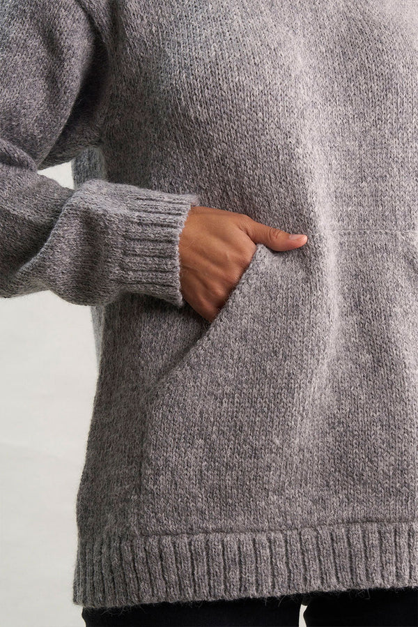 Person wearing a gray knitted sweater with a plain background
