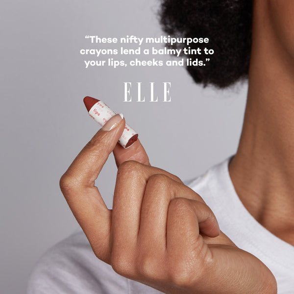 Hand holding a makeup crayon with 'ELLE' text on a gray background
