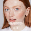 Close-up of a person with red hair and blue eyes, wearing a white shirt. Text overlay from 'ELLE' magazine.