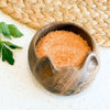Wooden cat-shaped bowl filled with pink salt on a textured surface.