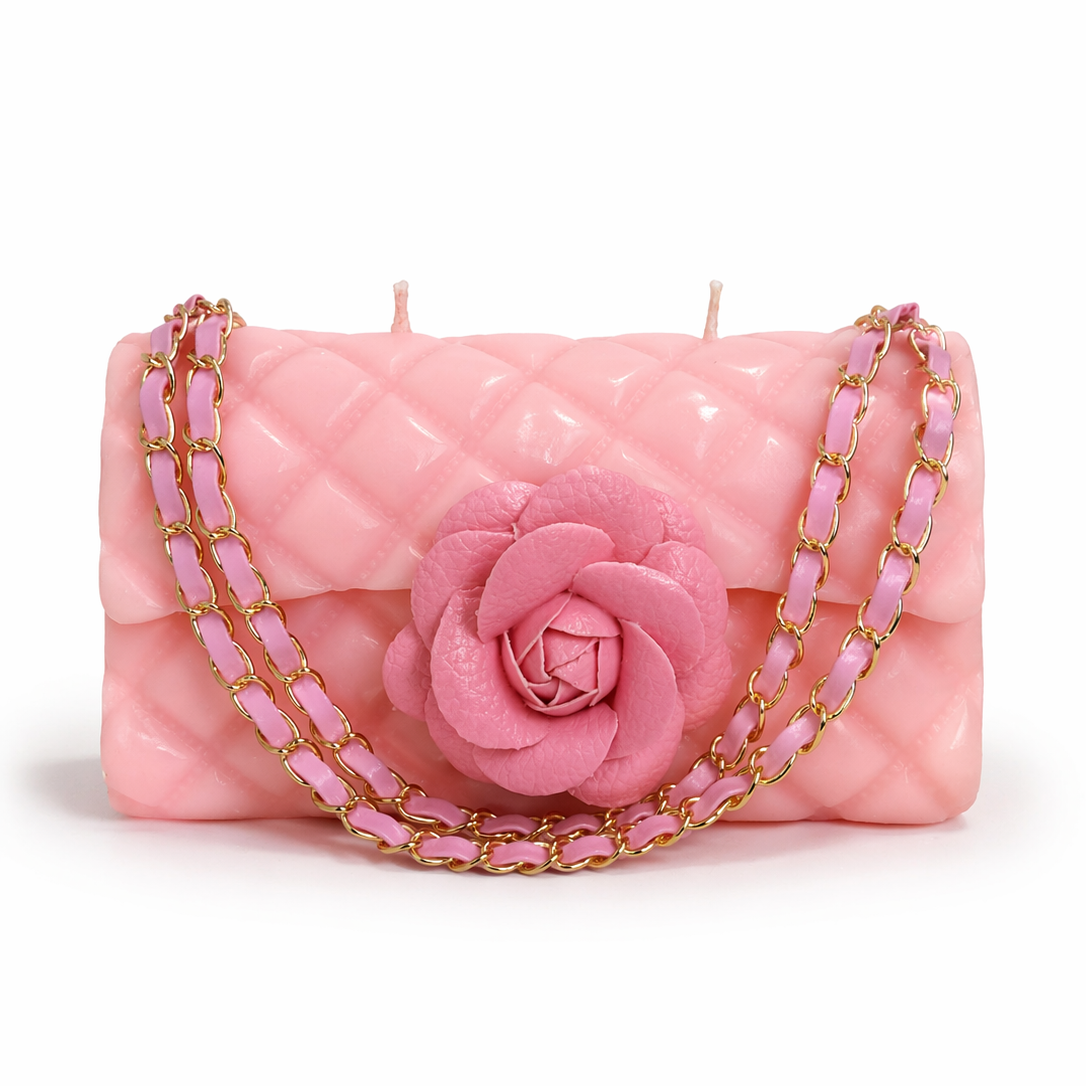 Pink candle shaped like a handbag with a rose and gold chain on a white background