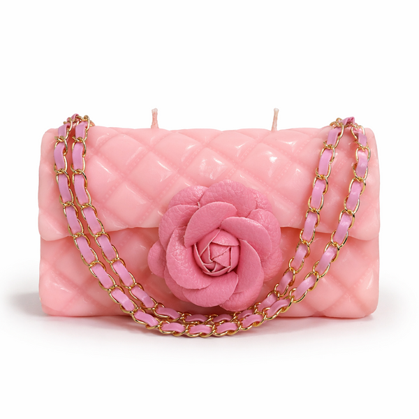 Pink candle shaped like a handbag with a rose and gold chain on a white background