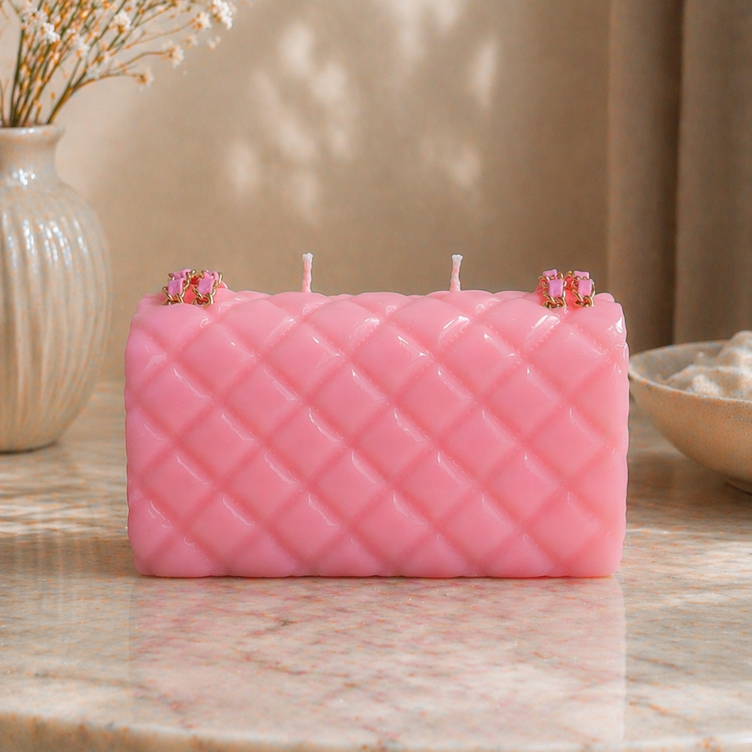 Pink quilted-pattern candle on a marble surface with decorative elements.