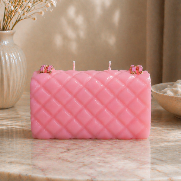 Pink quilted-pattern candle on a marble surface with decorative elements.