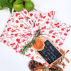 Gift wrapped in red and white patterned paper with a small chalkboard tag, surrounded by Christmas decorations.