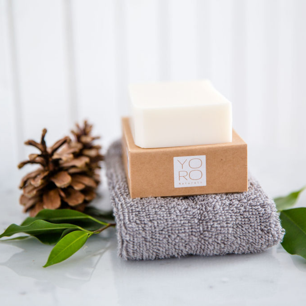 Bar of soap in a brown box with 'YORO' branding on a white surface with green leaves and a pine cone.