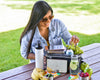 Woman at a picnic table with a cooler, food, and drinks in an outdoor setting