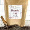 Bag of Bloomin' Soil with a trowel on a white tiled background