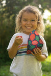 Child holding a colorful toy outdoors with greenery in the background