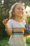 Child holding a red object and colorful bag outdoors with greenery in the background