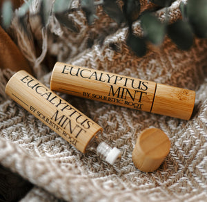 Two Soulistic Root eucalyptus mint bamboo essential oil rollers on a textured surface with fresh greenery in the background.