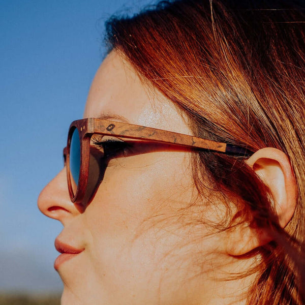 Close-up of a person wearing wooden sunglasses with a clear blue sky background